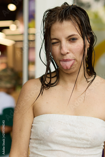 фотографія Portrait of a silly young woman with wet hair sticking out her tongue and winking, dressed in a white strapless lace top while celebrating a fun summer outdoor water festival