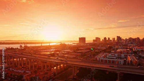 Warm sunlight dazzling the scenery of the city. Cars move by the Coronado Bridge at sunset. Port cranes in the backdrop. California, USA.