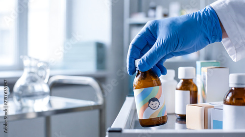 Medical professional in blue gloves picking up a bottle of pediatric medicine from a hospital cart