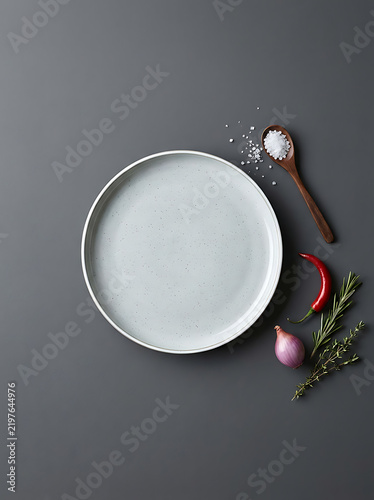 Minimalist white bowl with salt, pepper, and fresh herbs on neutral background for food blogging or recipe content