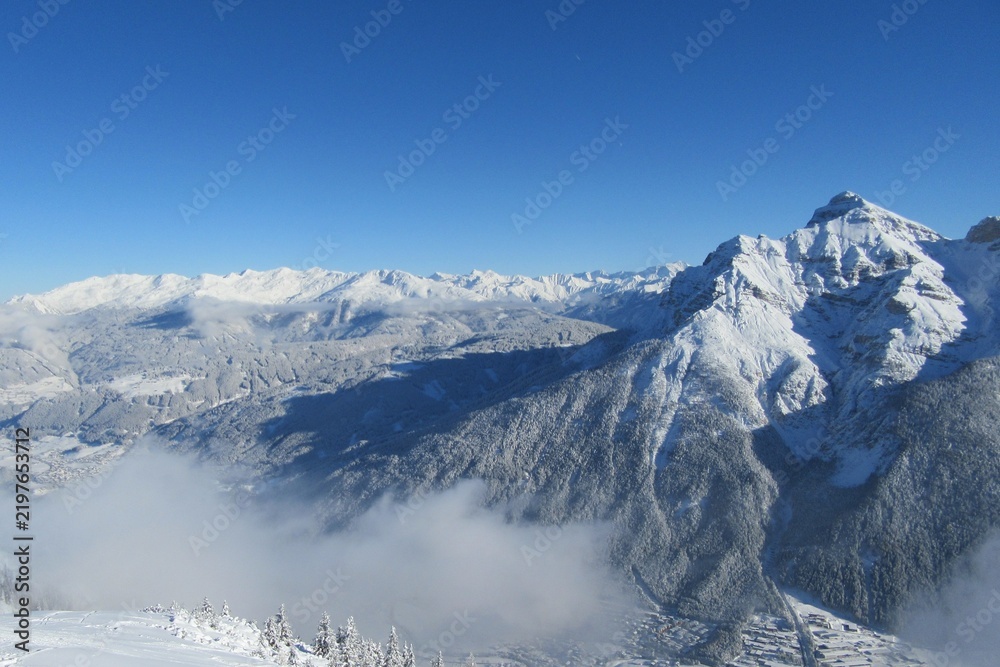 Obraz premium Snow covered mountain panorama, with a snow covered forest and snow covered valley in winter. Taken in Tirol, Austria. 