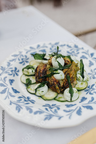 Crispy Fried Zucchini Flowers with Fresh Cheese and Herbs. Fried zucchini blossoms served with fresh cheese on a decorative ceramic plate. Mediterranean, Aegean and Italian-inspired seasonal cuisine. 