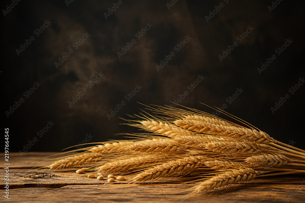 Obraz premium A close-up of several stalks of golden wheat resting on a rustic wooden surface against a dark, moody background.
