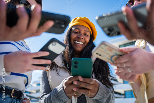 Outdoor lifestyle scene of a Black woman using a smartphone while surrounding hands hold phones and money, suggesting online payment and social finance.