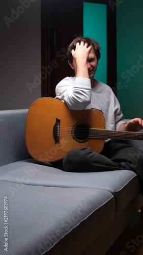 Vertical video musician sitting on a sofa covering his face with hands, experiencing stress and disappointment with his musical career, contemplating challenges