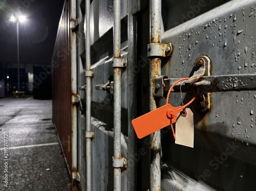 Canvastavla Orange security seal on rusty shipping container latch at night
