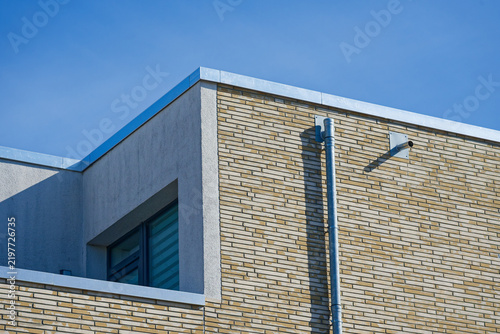 Modern building corner with brick wall and metal pipe under clear blue sky