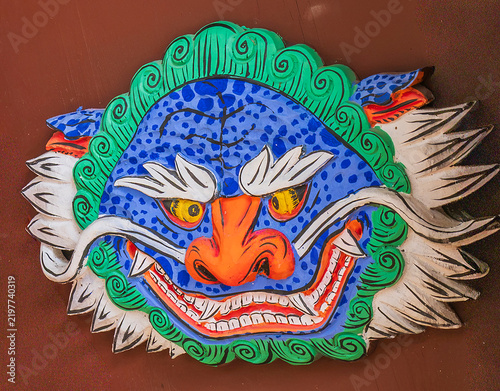 Traditional colorful painted wooden goblin mask carving with dragon face on temple building wall in South Korea.