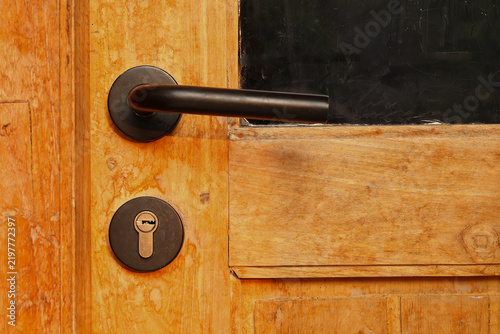 Close up of a modern black metal door handle and keyhole lock on a rustic wooden door, home architecture interior and security concept.