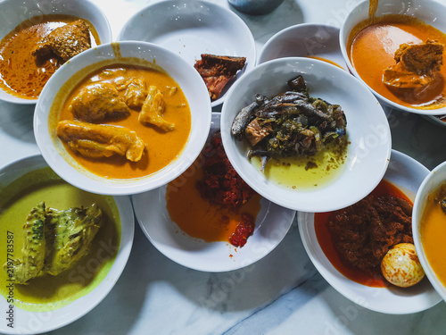 Assorted Minangkabau cuisine or Nasi Padang dishes served in small white bowls, including rendang, chicken curry, fish curry, dendeng balado, green chili with anchovies, and lado tanak with boiled egg
