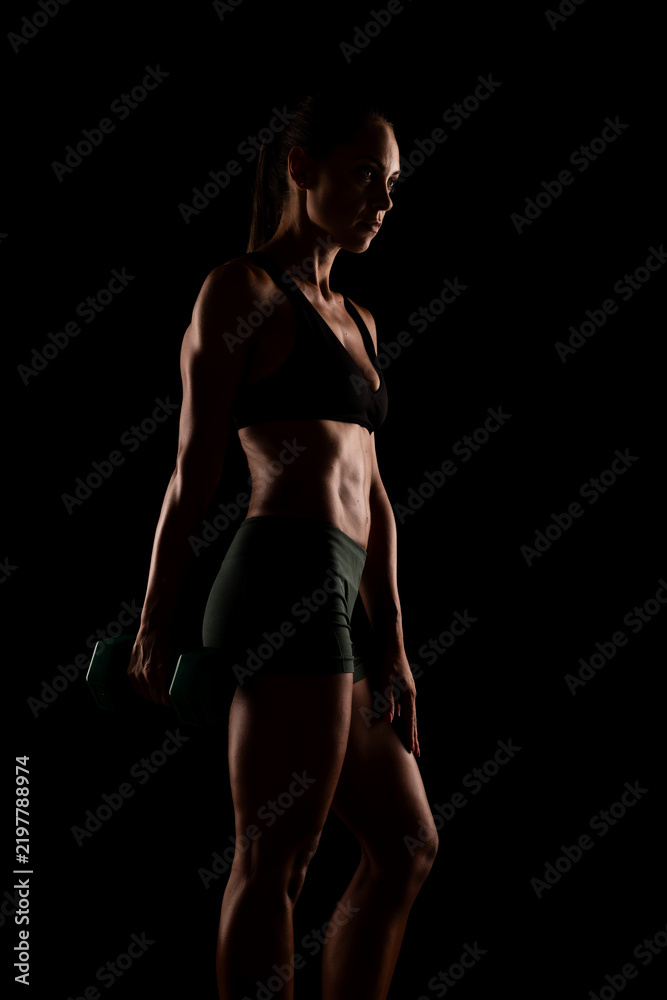 Fototapeta premium Side Profile of a Fit Woman Holding Dumbbells on a Dark Background