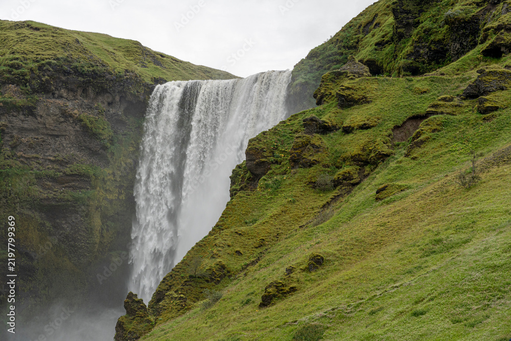 Fototapeta premium Powerful Waterfall Tumbling Over Mossy Green Cliffs