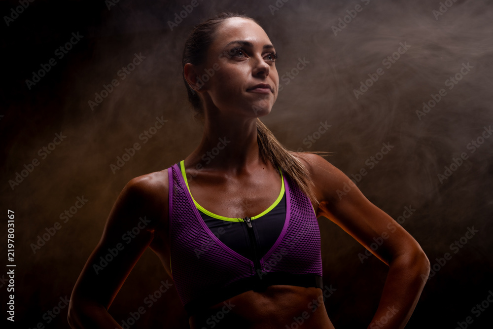 Obraz premium Strong and confident woman in athletic wear against a dramatic smoky background