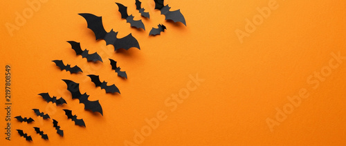 Black paper bats flying on orange background, Halloween party decoration