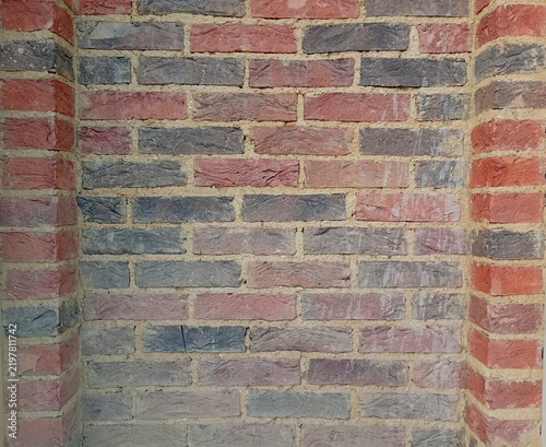 Fotografía A rustic multi-coloured brick wall texture with a decorative recessed niche design, featuring a combination of red, orange, and dark grey clinker bricks with thick textured concrete mortar joints