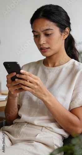 Woman using smartphone indoors with neutral attire and natural light