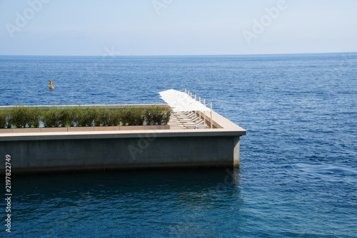 Bild auf Leinwand Modern seaside deck with a row of white sun loungers and umbrellas overlooking a vast blue sea under a pale, cloudless sky