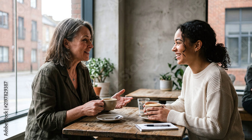 Two smiling women talking and drinking hot coffee together in a cozy cafe