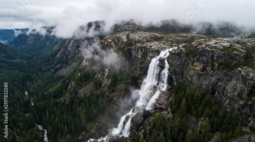 Mountain waterfall plunging through misty pine forest.
