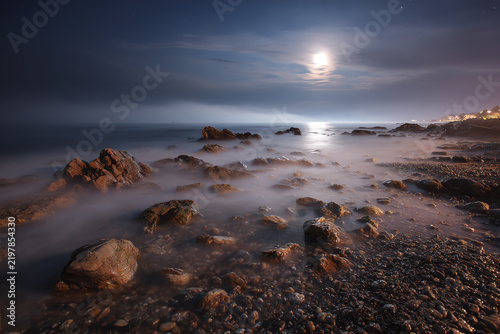 Moonlit Serenity on the Rocky Shore: A breathtaking long-exposure shot captures the tranquil beauty of a rocky coastline under a full moon.