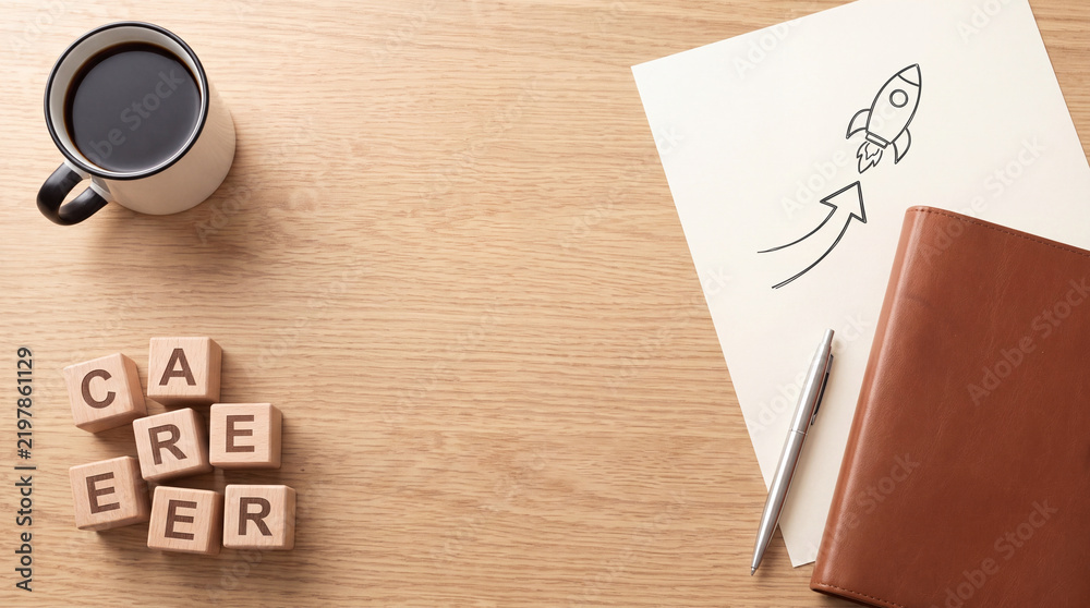 Obraz premium Business career growth and startup concept featuring wooden blocks spelling CAREER with a hand-drawn rocket on paper, leather notebook, pen, and a cup of black coffee on a light wooden desk surface.