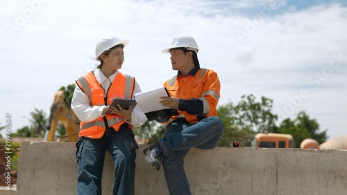 Принти на полотні Asian Civil Engineers Sitting on Concrete Barrier Consulting Blueprints and Digi