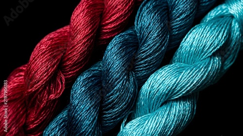 Close up of three colorful twisted silk threads on a black background.