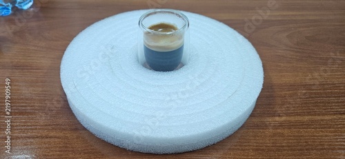 Glass cup of espresso placed in circular white foam ring on wooden table
