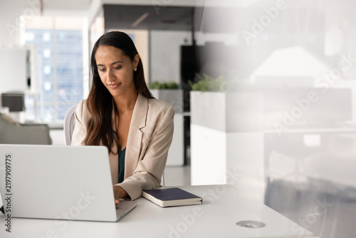 Businesswoman sits at office desk, working on project or corporate digital tasks, typing on laptop, responding on business emails, consulting clients or browsing. Administrative workflow management