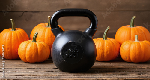 Heavy kettlebell with Halloween pumpkins on wooden background. Healthy fitness lifestyle autumn composition.
