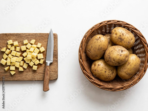 Fresh potatoes in wicker basket and diced potato cubes on wooden cutting board