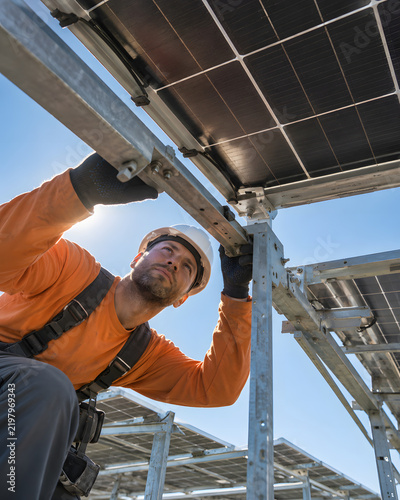 Technician inspecting solar panel hardware from a dramatic underside perspective.