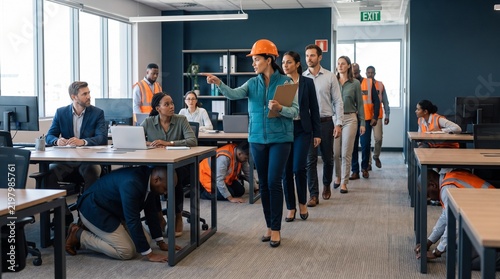 Workers in safety helmets practicing earthquake emergency drill in modern office environment