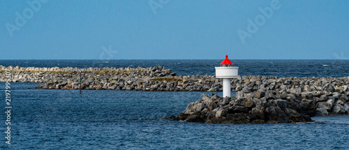 Small white and red nautical beacon on a stone breakwater in the blue ocean with copy space
