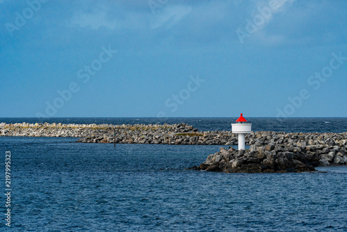 Small white and red nautical beacon on a stone breakwater in the blue ocean with copy space
