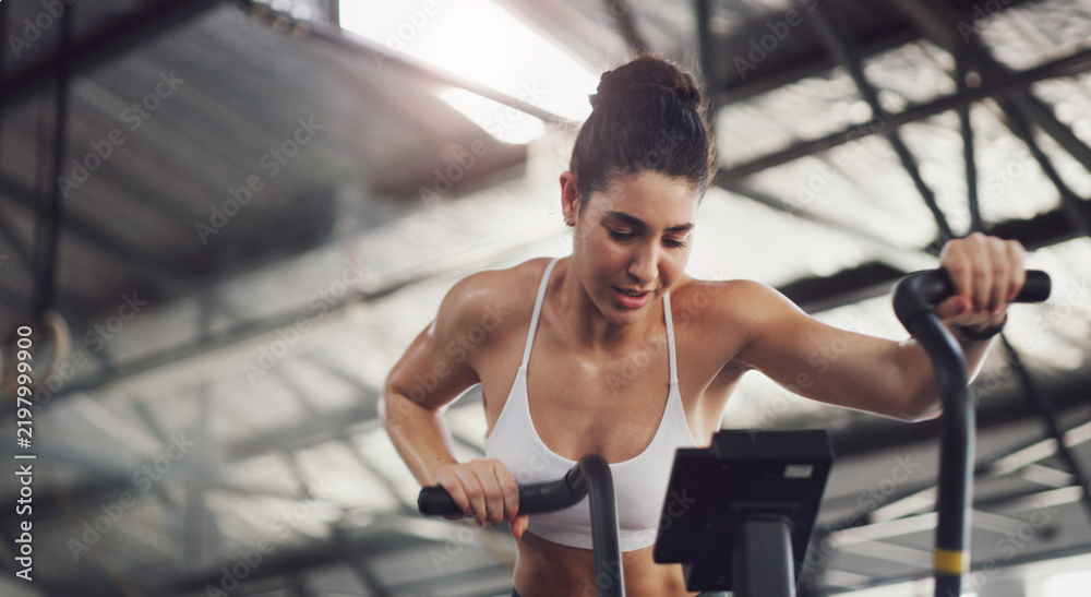 Fototapeta premium Workout, woman and gym with stationary bike, cardio training and burning calories for wellness. Fitness, athlete and cycling challenge on exercise bicycle for health routine, sweating and endurance