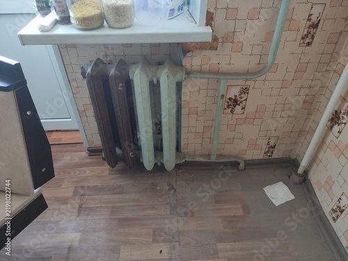 Old cast iron radiators with green and brown paint on wooden floor in kitchen