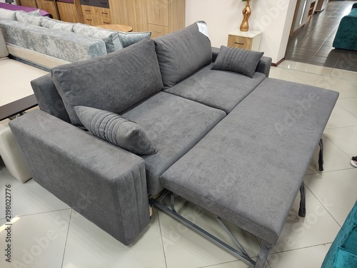 Grey fabric sofa bed with extended sleeping section and pillows in a furniture store