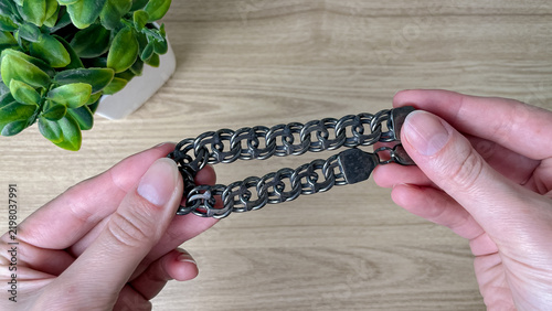 Obraz na plátně A pair of female hands examines a darkened silver chain featuring large, interlocking links and a clasp
