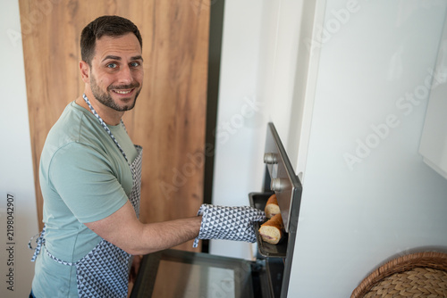 Fotografie Happy man baking bread rolls in kitchen oven