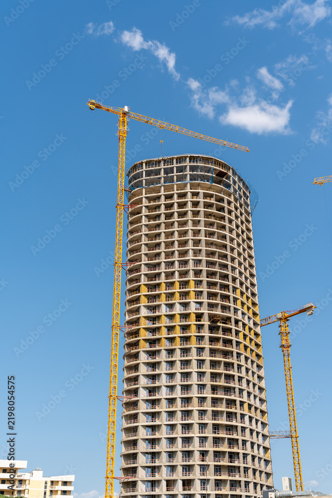 Fototapeta premium Modern high-rise building under construction with cranes against a blue sky