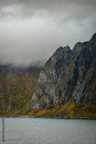 Majestic rocky mountain peak covered in fog rising from ocean water in northern scandinavia with copy space
