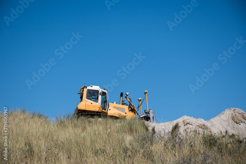Excavator working in coastal dunes during sand nourishment on Ameland, Netherlands, coastal protection, beach maintenance, erosion control, climate adaptation, heavy machinery, construction.