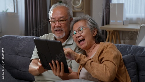 Принти на полотні Excited senior Asian couple look at a tablet as the elderly woman points at the screen, showing digital discovery, online entertainment, shared excitement and happy retirement at home