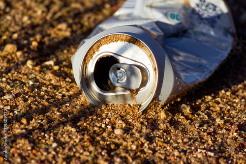 Discarded crushed aluminum beverage can lying on gritty sandy beach ground, creating an environmental pollution hazard close-up view capturing the impact of human litter on nature outdoors
