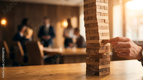 Person playing wooden block tower game in office meeting