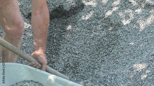 Shovel pouring crushed stone into a wheelbarrow on a construction site. Close-up of a worker's hands with a shovel pouring small gravel into a wheelbarrow, hard physical labor and construction work