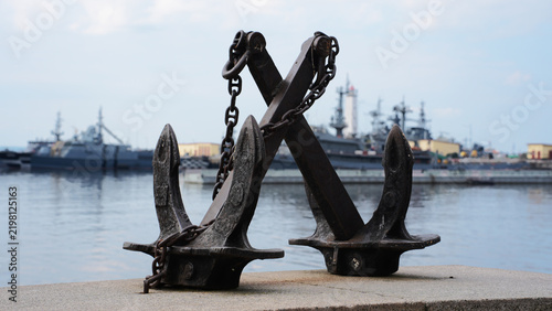 Old ship anchors with chains on the pier against warships background