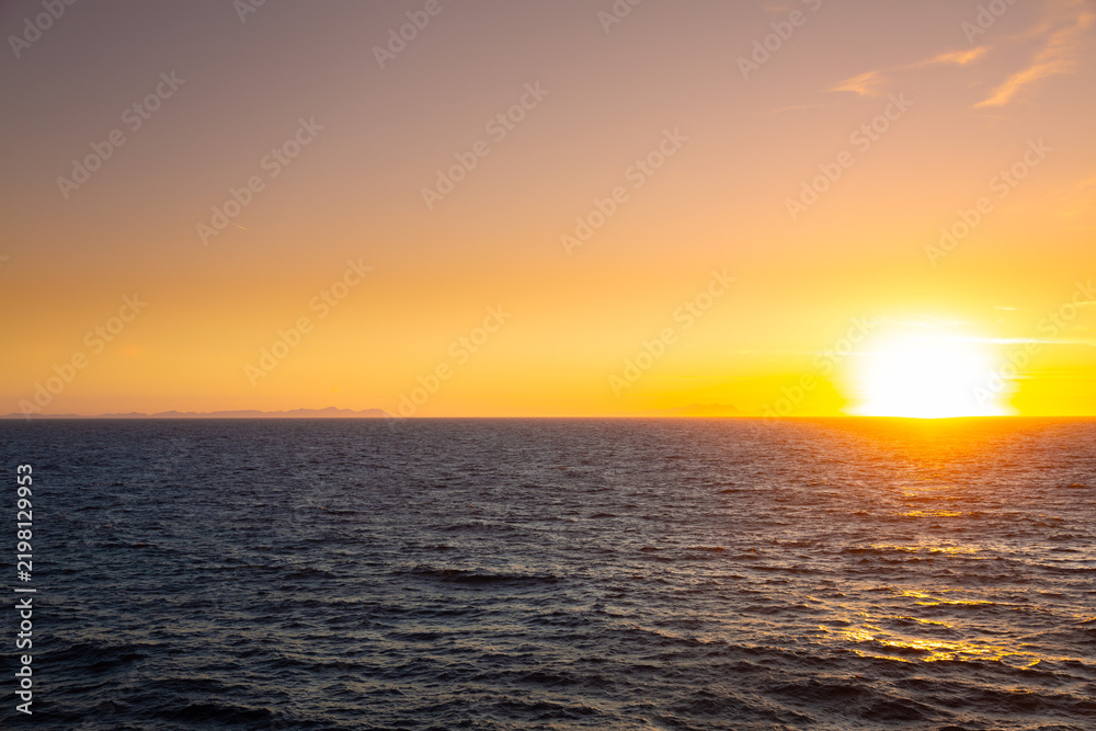 Fototapeta premium Golden sun setting over ocean horizon and coastal structures