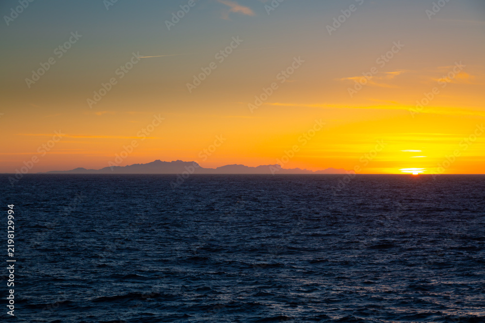 Fototapeta premium Golden sun setting over ocean horizon and coastal structures